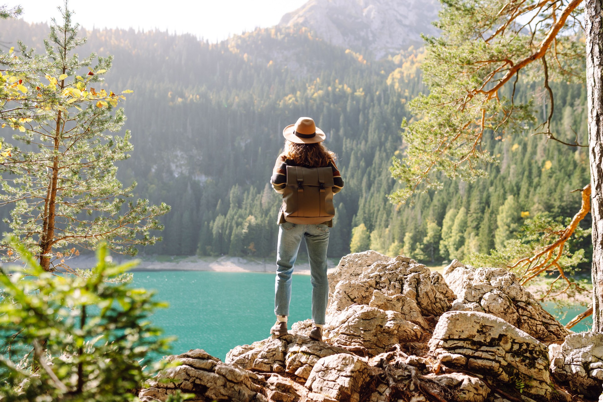 Enjoying a peaceful moment, a woman sits on a rocky ledge while gazing at the stunning turquoise lake surrounded by lush mountains during daylight.